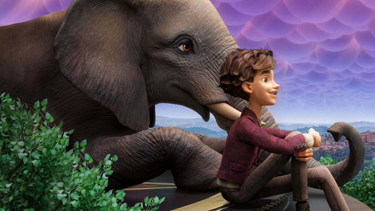 a boy sitting with an elephant on a hill above a city